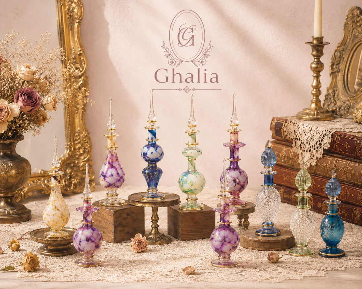 A styled collection of vintage-inspired glass perfume bottles in various colors and patterns, displayed on wooden stands against a warm beige background with antique books, a gold mirror, and dried flowers. The brand logo 'Ghalia' is visible in the center.